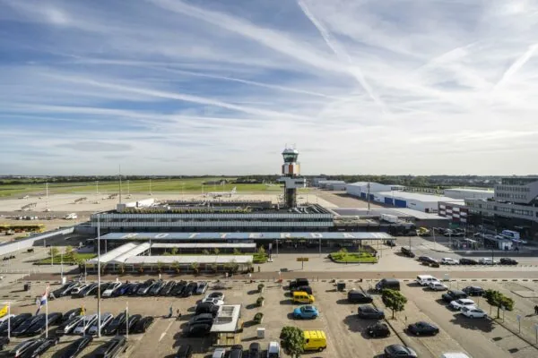 Luchtfoto van Rotterdam The Hague Airport met terminals, verkeerstoren en parkeerterrein op de voorgrond.
